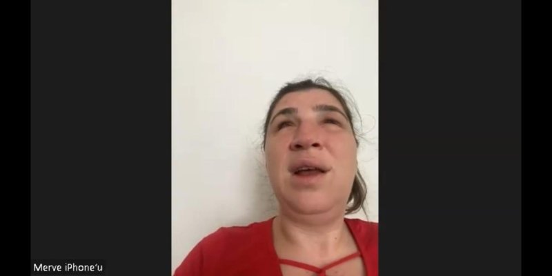 Ekranda kırmızı buluz giymiş konuşmacının yüzü görünüyor, konuşuyor. Arka planda beyaz duvar var.