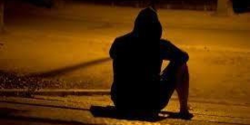 Gece sokak ortasında sarı ışıklı sokak lambasının ışığının altında arkası dönük şekilde yerde bir kadın oturuyor.
