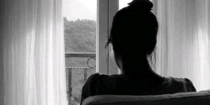 Siyah-beyaz fotoğrafta, bir kadın pencerenin önünde oturuyor. Saçları topuz yapılmış. Pencerenin önünde bir masa var ve masanın üzerinde bir fincan duruyor. Pencerenin dışında, hafifçe görünen bir doğa manzarası var; ağaçlar ve uzakta dağlar seçilebiliyor.