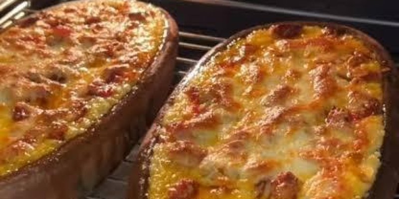 Fırın rafı üzerinde duran, içi dolgulu iki adet yarım kabak teknesi. Görüntü fırının içinden alınmış. Orta rafta yan yana duran iki yarım kabak var; dış kabukları koyu yeşil, iç kısımları oyulmuş ve üstleri eritilmiş peynirle kaplı. Peynirin üzerinde yer yer kızarmış kahverengi noktalar ve küçük kırmızı parçalar görülüyor. Sol taraftaki kabak daha büyük ve daha dolgun; sağdaki biraz daha küçük. Üst yüzeylerde parlak yağlı bir görünüm var ve kenarlarda hafif kararma mevcut.