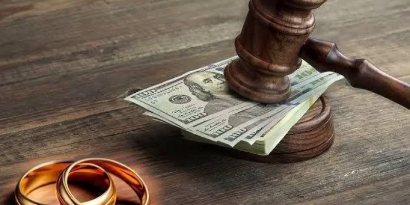 Ahşap bir masa üzerinde bir yargıç tokmağı, bir deste Amerikan doları ve 2 altın yüzük. Yargıç tokmağı, deste halindeki dolarların üzerine yerleştirilmiş. Yüzükler tokmağın ve paraların sol tarafında duruyor.
