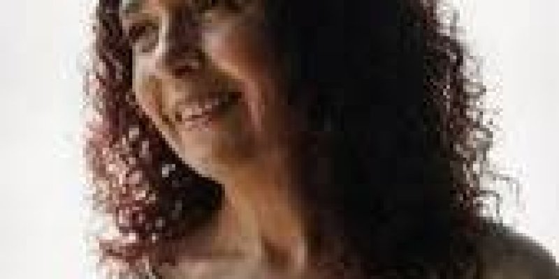 Bilgesu Erenus’un kıvırcık koyu kestane saçlı portresi. Ten rengi buğday ile açık esmer arasında. Omuz hizasında, doğal dalgalı ve kabarık saçlı ve saçları yüzünü çerçeveliyor. Başını hafifçe sağ tarafa çevirmiş, yumuşak bir gülümsemeyle uzak bir noktaya bakıyor. Yüz ifadesi sakin ve huzurlu; yanaklarında hafif gülümseme çizgileri belirgin. Üzerinde açık renkli, krem tonlarında bol bir bluz; yakasında ince bir işlemeli veya desenli şerit dikkat çekiyor.
