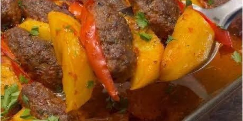 Dikdörtgen cam fırın kabında köfte, patates ve biberle hazırlanmış sulu bir yemek. Köfteler uzun, hafif oval şekilli ve kızarmış kahverengi renkte. Aralarına kalın dilimlenmiş sarı patatesler ve uzunlamasına kesilmiş kırmızı biberler dizilmiş; hepsi sıralar halinde düzenli bir şekilde yerleştirilmiş. Yemeğin dibinde kırmızımsı, yağlı ve hafif sulu bir sos tabakası; sos, baharatlı ve domatesli. Üzerine ince kıyılmış taze yeşillikler, maydanoz serpiştirilmiş. Sağ tarafta metal bir servis kaşığı, b