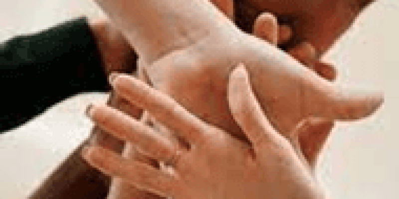 Farklı ten renklerine sahip birkaç kişinin elleri bir araya getirilmiş. Eller birbirine üst üste konmuş ve birlik, takım çalışması veya dayanışma hissi veriyor. Odak noktası birleşen eller.