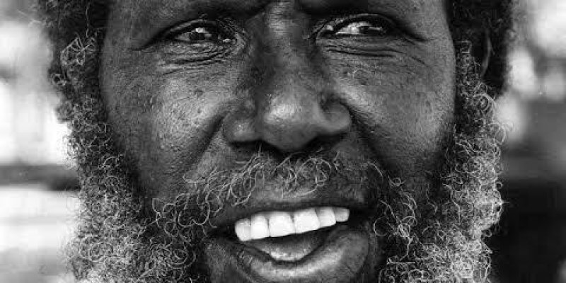Kıvırcık sakallı Eddie Koiki Mabo, siyah-beyaz portresi. Koyu tenli, kısa ve gür kıvırcık saçlı. Ağız hafifçe açık, dişleri görünüyor ve ifadesi sanki konuşuyormuş ya da gülümsüyormuş gibi canlı. Gözleri hafif kısık, bakışı ileriye doğru yönelmiş. Çenesinden aşağı doğru uzanan uzun, dalgalı ve yer-yer beyazlamış sakalı, boynunda havluya benzeyen kalın bir kumaş dolanmış; omuzlarının üst kısmı ve giysisinin küçük bir bölümü kadraja giriyor.