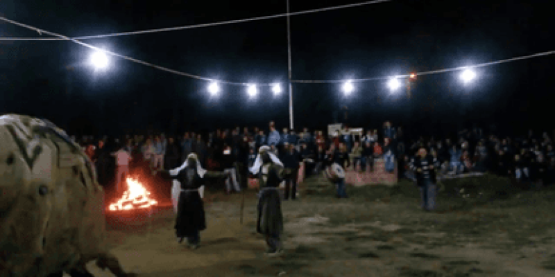 Gece direkler üzerindeki lambalarla aydınlatılmış kırsal bir meydanda toplanmış köy halkı var. Meydanın ortasında ateş yakılmış. Ateşin yanında beyaz uzun başörtülü, köylü kıyafetli iki kadın kolları açık şekilde karşılıklı oynuyorlar. Kadınların arkasında davul çalan bir adam görünüyor.