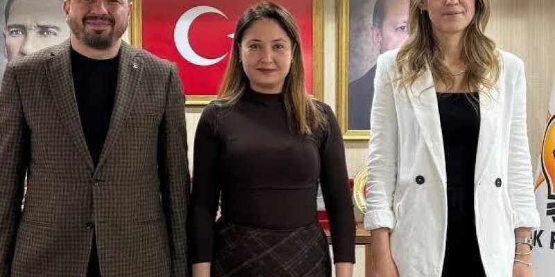 Üç kişi yan yana duruyor. Solda, kısa saçlı, sakallı, orta yaşlarda bir erkek, açık tenli. Koyu renk bir tişörtün üzerine kahverengi-kareli bir ceket giymiş. Hafifçe gülümsüyor, kolları iki yanında duruyor. Ortada, omuz hizasında düz saçlı, açık tenli bir kadın, koyu kahverengi, uzun kollu, boğazlı bir üst giymiş. Altında koyu renkte, çapraz desenli bir etek, bileklerinde saat ve bileklikler. Nötr bir ifadeyle kameraya dönük duruyor. Sağda, omuzlarından biraz aşağı dökülen dalgalı saçlı, açık te