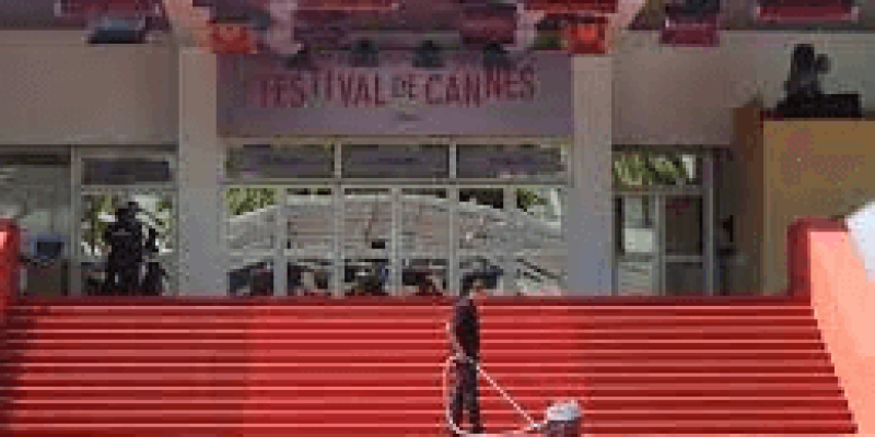 Büyük bir binanın önünde kırmızı halılı çok uzun ve geniş merdivenler var. Binanın giriş kapısının üst kısmında “Festival de Cannes” yazıyor. Bir erkek elektrik süpürgesi ile merdivenleri temizliyor.