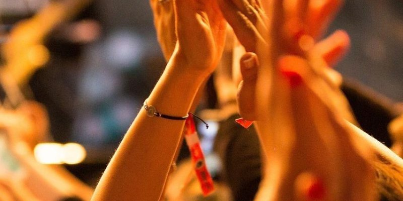Işıklarla aydınlanmış bir ortamda havaya kalkmış birçok insan eli alkış tutuyor.