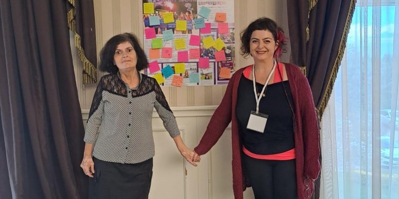 Altın rengi püsküllü siyah iki perdenin arasında boyuna çizgili duvar kağıdı kaplı arka zemin var. Duvar kâğıdı üzerine "Kadın Haber " sayfasının büyütülmüş hali üzerinde rengarenk 'postitlere notlar yapıştırılmış. Solda siyah, diz hizasındaki etek üzerine ,gri, yakası siyah tülle süslenmiş bluzu, siyah küt saçlarıyla hafifçe tebessüm ediyor. Sağda siyah saçlarının bir kısmını pembeyle renklendirmiş; siyah tayt ve bluz içine pembe askılı kıyafetiyle gülen bir kadın birlik olmanın gücün