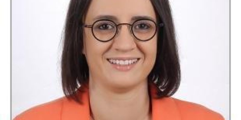 Kısa saçlı, gözlüklü, üzerinde turuncu ceket olan bir kadın.
