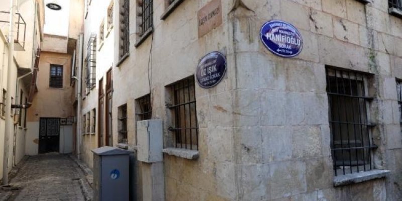 Dar, taş döşeli bir sokak arasında köşede duran eski bir taş binanın zemin ve üst kat pencerelerinde siyah demir parmaklıklar, duvarları açık bej renkli taşlardan oluşuyor. Köşe duvarında iki mavi beyaz yuvarlak sokak tabelası ile bir de dikdörtgen taş levha. Üstteki taş levhada “GÜVERCİN GEÇİDİ” yazıyor. Hemen altında, köşe duvarın sağ yüzünde duran yuvarlak mavi tabelada “HANİFOĞLU SOKAK” yazısı, üzerinde “ŞEHİTKAMİL BELEDİYESİ / ŞEHİTKAMİL” ibaresi. Diğer yuvarlak mavi tabelada “ÖZ IŞIK HANIF