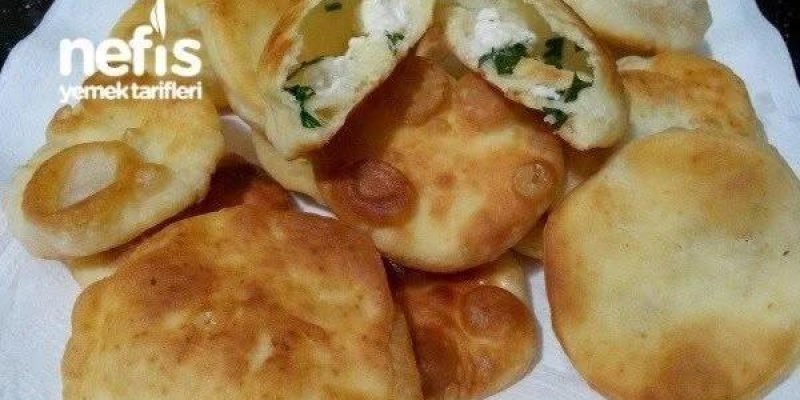 Tabakta kâğıt havlu üzerinde duran, altın rengi kızarmış hamur işleri. Hamurlar yuvarlak ve hafif kabarık, bazılarının yüzeyinde kızarmış yuvarlak kabarcıklar. Üst tarafta bir tanesi ortadan ikiye kesilmiş; içi beyaz peynir ve yeşil otlu bir harçla dolu. Hamurların rengi açık sarıdan daha koyu altın kahverengiye doğru değişiyor ve hepsi evde kızartılmış poğaça veya pişi görünümünde.