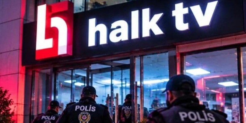 Gece vakti, giriş kapısının üzerinde siyah zeminde parlak beyaz harflerle “halk tv” yazan bir tabela; solda kırmızı zeminde beyaz bir logo. Ön planda koyu üniformalı birkaç polis sırtlarında beyaz harflerle “POLİS” yazısı ve armaları, binaya doğru ilerliyor.
