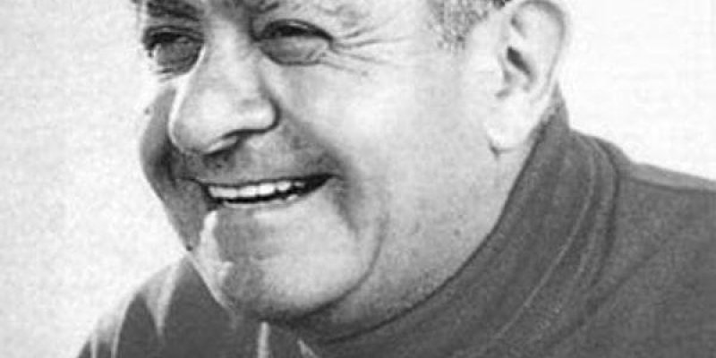 Ahmed Arif’in siyah-beyaz bir portre fotoğrafı. Yakın planda, başı hafif sola dönük şekilde gülümsüyor. Saçları geriye taranmış ve tepe kısmı seyrek. Yüzünde gülümsemeye bağlı çizgiler belirgin. Koyu renk, boğazlı bir kazak giymiş. Arka plan düz ve açık tonlu.