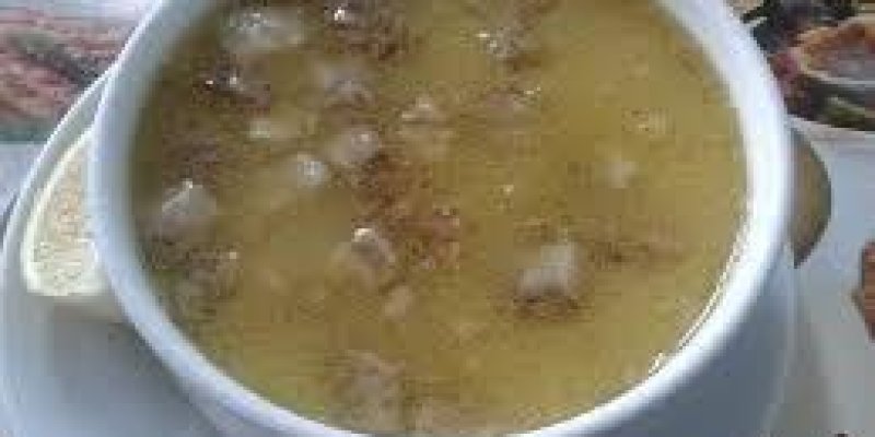 Beyaz yemek masası üzerinde beyaz bir çorba kâsesinde üzerinde kıtır ekmek olan mercimek çorbası var.
