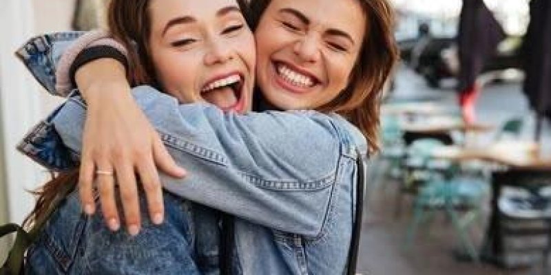 İki genç kadın birbirlerine sıkıca sarılmış gülümsüyor. İkisi de açık kahverengi tonlarında saçlı ve açık tenli. Yüzleri birbirine çok yakın, gözleri kapalı ya da yarı kapalı, ifadeleri çok neşeli. Üzerlerinde açık mavi kot ceketler birbirine oldukça benziyor. Soldaki kadının ağzı açık şekilde gülüyor, parmağında ince, sade bir yüzük. Sağdaki kadının dudakları kapalı ama geniş bir gülümsemesi var.