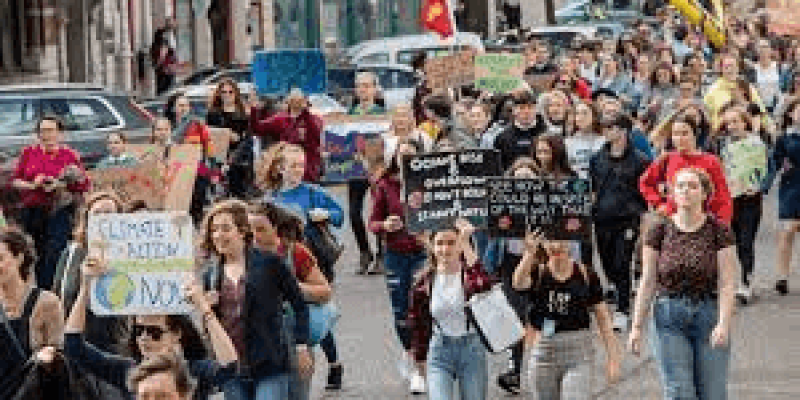 Bir grup insan sokakta yürüyüş yapıyor. Ellerinde çeşitli pankartlar taşıyorlar ve bazı pankartlarda "Climate Action Now" ve "Oceans are rising and so are we" gibi İngilizce çevre ile ilgili sloganlar yazıyor. İnsanlar genç ve aktivist bir grup. Yürüyüşe katılanlar kararlı ve ciddi.