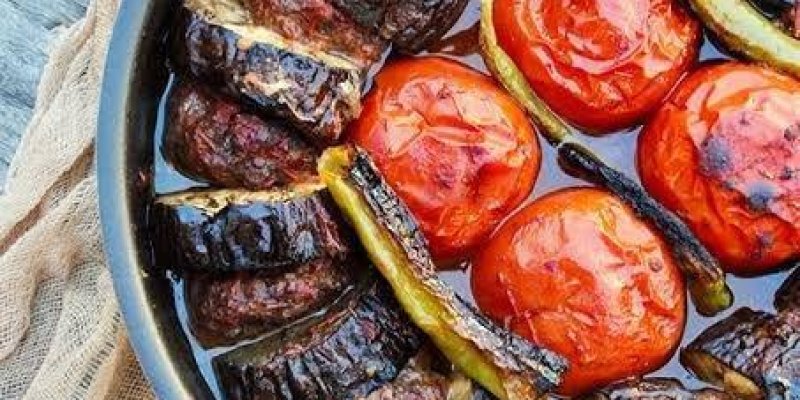 Bir tencere içinde pişirilmiş dilimlenmiş patlıcan, köfte, domates ve biberlerden oluşan yemek. Patlıcan dilimleri ve köfteler sırayla dizilmiş, aralarına bütün domatesler ve biberler yerleştirilmiş. Yemeğin üzeri hafif kızarmış. Tencere, bir bez örtü üzerinde duruyor.