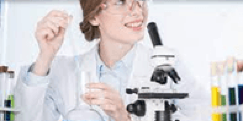 Laboratuvar ortamında mikroskobun arkasında orta yaşta saçlarını topuz yapmış gözlüklü bir kadın var. Kadın tek eliyle içinde mavi sıvı olan beher (laboratuvarda içine kimyasal sıvıların konulduğu şişe) tutuyor.