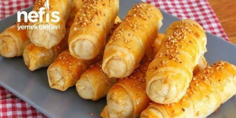 Gri bir tabak üzerinde üst üste dizilmiş sigara börekleri. Böreklerin üzeri altın sarısı renginde ve üzerlerine susam serpilmiş. Tabak, kırmızı ve beyaz kareli bir örtünün üzerinde duruyor. Sol üst köşede "nefis yemek tarifleri" yazısı bulunuyor. Börekler oldukça iştah açıcı görünüyor.