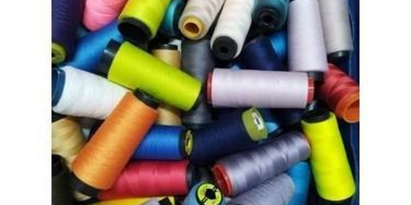 Mavi plastik bir kutunun içinde birçok renkte büyük dikiş ipliği makarası. Kutunun içine gelişigüzel yerleştirilmiş, üst üste duruyorlar. Görünen başlıca renkler arasında açık ve koyu pembe, parlak sarı, limon yeşili, turkuaz, lacivert, mor, turuncu, açık mavi, gri, krem ve beyaz tonları. Makaraların çoğunun ortası siyah plastik, bazıları kırmızı veya koyu renk uçlara sahip. İplikler genelde kalın ve parlak görünümlü, endüstriyel veya overlok makinelerinde kullanılan büyük bobinlere benziyor. Ar