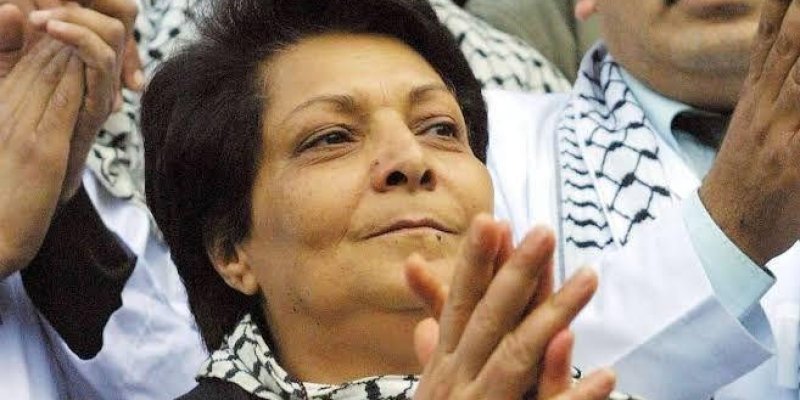 Ön planda Leyla Halit’in elleri alkışlar şekilde. Kısa siyah saçlı ve boynunda siyah-beyaz desenli bir atkı bulunuyor. Arkasında, benzer desenli atkılar takan başka insanlar da var. Bu kişilerden biri, bıyıklı bir erkek sağ tarafta. bir etkinlikte ya da toplantı fotoğrafı. Yüz ifadesi ciddi ve odaklanmış.