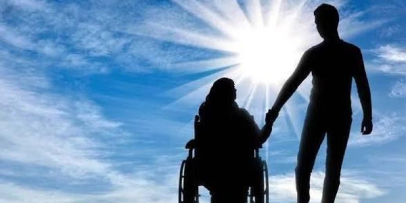 Tekerlekli sandalyede oturan bir kişi ve yanında ayakta duran başka bir kişi silüet hâlinde.Tekerlekli sandalyedeki kişi ortada, oturur pozisyonda; diğer kişi sağ tarafta ayakta duruyor ve eliyle sandalyedeki kişinin elini tutuyor.