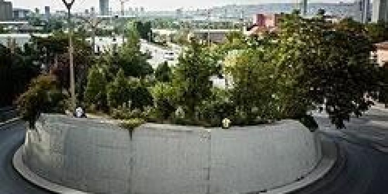 Yuvarlak bir ada etrafında dönen araç yolu. Beton bir duvarla çevrili adanın üstü yoğun yeşil ağaçlar ve çalılarla kaplı, küçük bir koruluk gibi duruyor. Ada etrafındaki asfalt yol tek şeritli, duvarın iki yanında trafik levhaları.