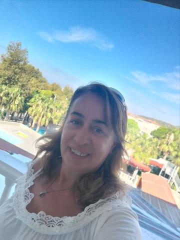 Arkasında yeşil alan olan balkonda yakaları fistoyla süslenmiş açık omuzlu bluzuyla gülümsüyor. Açık kumral saçlarına güneş gözlüğü takmış.