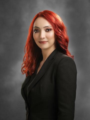 Alev kırmızısı dalgalı, uzun saçları, siyah ceketiyle ayakta gülümsüyor.