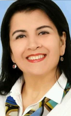 Gülen bir portre. Koyu renk, düz ve omuz hizasında saçları var. Kırmızı ruj sürmüş ve hafif bir makyaj yapmış. Küçük yuvarlak küpeleri dikkat çekiyor. Üzerinde beyaz bir gömlek ve renkli, mavi ağırlıklı bir fular var. Arka plan tek renk, açık mavi.