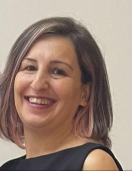 Omuzlarına yakın kısa küt kesimli saçlarıyla, içten gülümsüyor.