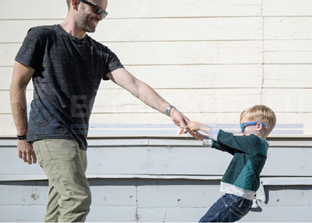  alanda orta yaşlı bir baba ile 4-5 yaşlarında bir oğlan çocuğu karşılıklı olarak duruyorlar. Çocuk,  babanın sol elini iki eliyle çekiştiriyor. İkisinde de gözlük var. Baba çocuğa gülümseyerek bakıyor. 