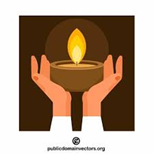 Bilekten yukarısını havaya kaldırmış iki elin arasında kahverengi bir kâsenin içinde yanan bir mum var.