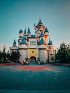 Çizgi fimlerde görülen büyük mavi çatılı beyaz şato maketinin önünde duran birkaç insan var.