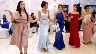 Bir düğün salonunda, şık abiye elbiseler giymiş beş genç kadın el ele tutuşarak halay çekiyor. Kadınlardan biri açık pembe kısa kollu bir elbise giymiş, elinde pembe bir mendil tutuyor. Yanındaki kadın açık mavi, askılı ve uzun bir elbise giymiş. Ortadaki kadın koyu mavi, dantel detaylı uzun bir elbise giymiş ve elinde beyaz bir mendil var. Dördüncü kadın kırmızı, omuzları açık uzun bir elbise giymiş. En sağdaki kadın pembe, straplez ve uzun bir elbise giymiş, elinde dantel bir mendil tutuyor. Arka planda b