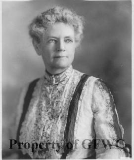 Siyah beyaz Etta Palm d'Aelders’in portresi. Dalgalı ve kısa gri saçlı, yüzü ciddi ve hafifçe gülümsüyor. Üzerinde yüksek yakalı, dantel detaylı ve desenli bir bluz var. Bluzun üzerinde koyu renkli iki şerit dikkat çekiyor. Arka plan sade ve flu. Görüntünün alt kısmında büyük harflerle "Property of GFWC" yazısı yer alıyor.