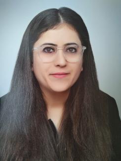 Koyu renk uzun ve düz saçlı, açık tenli Ekin Yılmaz. Yüzünde hafif bir gülümseme var. Gözleri koyu renkli ve gözlük takıyor; gözlüğü şeffaf çerçeveli. Üzerinde koyu renkli bir üst var ve arka plan açık, düz bir renkte. Fotoğraf vesikalık tarzında çekilmiş.