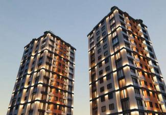 İki adet yüksek katlı, modern apartman binası. Binalar birbirine paralel şekilde duruyor ve her iki binanın dış cephelerinde aydınlatmalar bulunuyor. Cephelerde dikdörtgen şeklinde pencereler ve balkonlar dikkat çekiyor. Binaların üst katlarında çatılar hafif eğimli ve köşe detayları mevcut. Gökyüzü açık ve gün batımı ya da gün doğumu olduğu hissi uyandıran yumuşak bir ışık var.