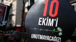 Yuvarlak, siyah bir pankart. Üzerinde kırmızı ve beyaz harflerle "10 EKİM'İ UNUTMAYACAĞIZ!" yazıyor. Yazının tam ortasında bir tel örgü ve onun üzerinde beyaz bir karanfil yer alıyor. Arka planda bulanık bir şekilde insanlar ve diğer pankartlar görülüyor. Bu pankart, 10 Ekim Ankara Garı katliamını anmak için yapılmış bir etkinlikte taşınıyor.