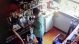 Mutfakta bir kişi, mutfak tezgahının önünde ayakta duruyor ve bir şeylerle meşgul. Etrafında çeşitli mutfak eşyaları, raflarda kavanozlar ve üstte bardaklar var. Sağ tarafta bir pencere var ve tezgâhın üzerine bol miktarda gün ışığı vuruyor. Kişinin üzerinde açık renkli bir üst var, alt kısmı karanlık renkte.