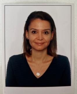 Kısa kahverengi saçlı Elif Eseroğlu, beyaz bir arka plan önünde poz veriyor. Koyu renkli bir kazak giymiş ve boynunda yuvarlak bir kolye takıyor. Hafif bir gülümsemesi var ve doğrudan kameraya bakıyor. Kulaklarında küçük küpeler bulunuyor.