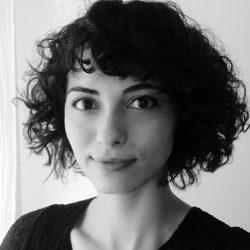 Kısa, dalgalı siyah saçlarıyla siyah-beyaz bir fotoğrafta umutlu bakıyor.