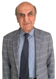 Gri ceketi, içinde mavi kareli gömleği ve lacivert üzerine açık renk kutucuk desenli kravatıyla. Gri, biraz dökülmüş saçlarıyla gülümsüyor.