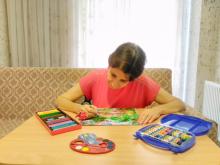 Yazarımız kırmızı tişörtüyle masada oturmuş. Kuru, sulu ve pastel boyalarla birlikte resim yapıyor.