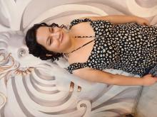 Topuzu, yanlarında bırakılmış dalgalı zülüfleriyle, siyah üzerine beyaz çiçekli askılı elbisesiyle tebessüm ediyor.